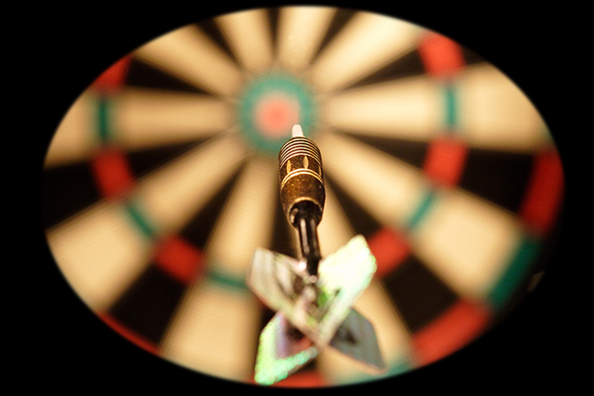 Das Bild zeigt einen Dartpfeil im Flug auf eine Dartscheibe. 