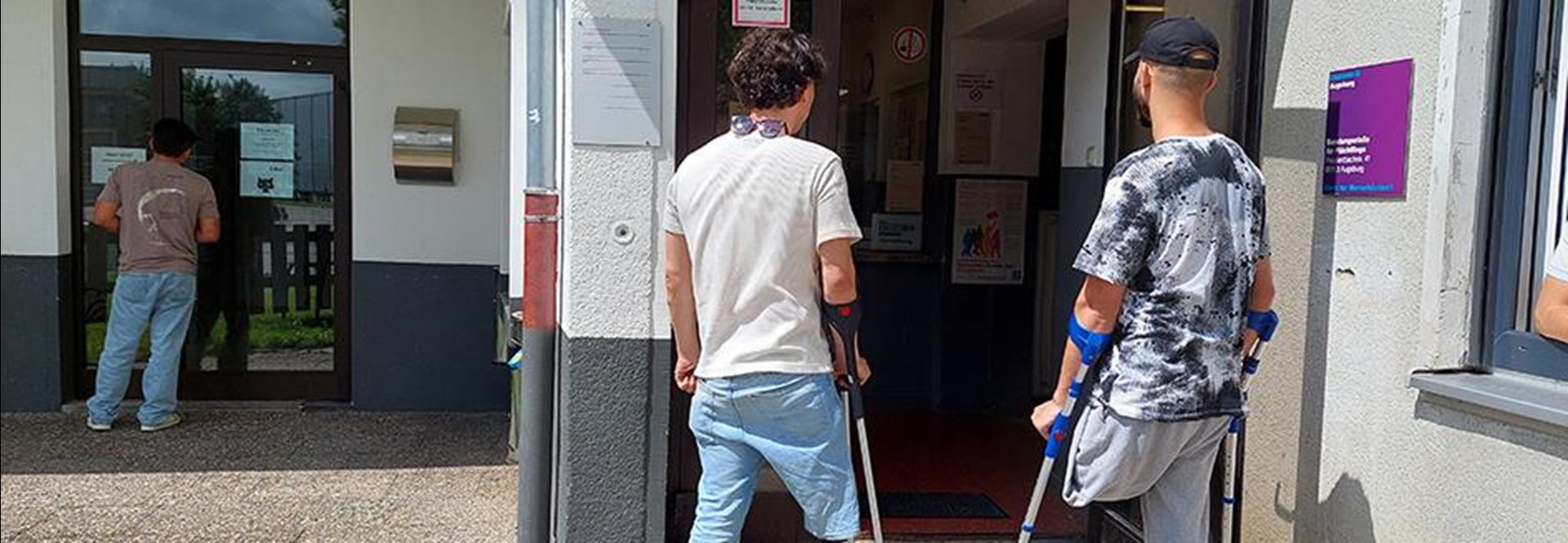 Das Bild zeigt zwei Männer von hinten, die vor einer Tür stehen. Beide Männer haben eine Beinprothese.