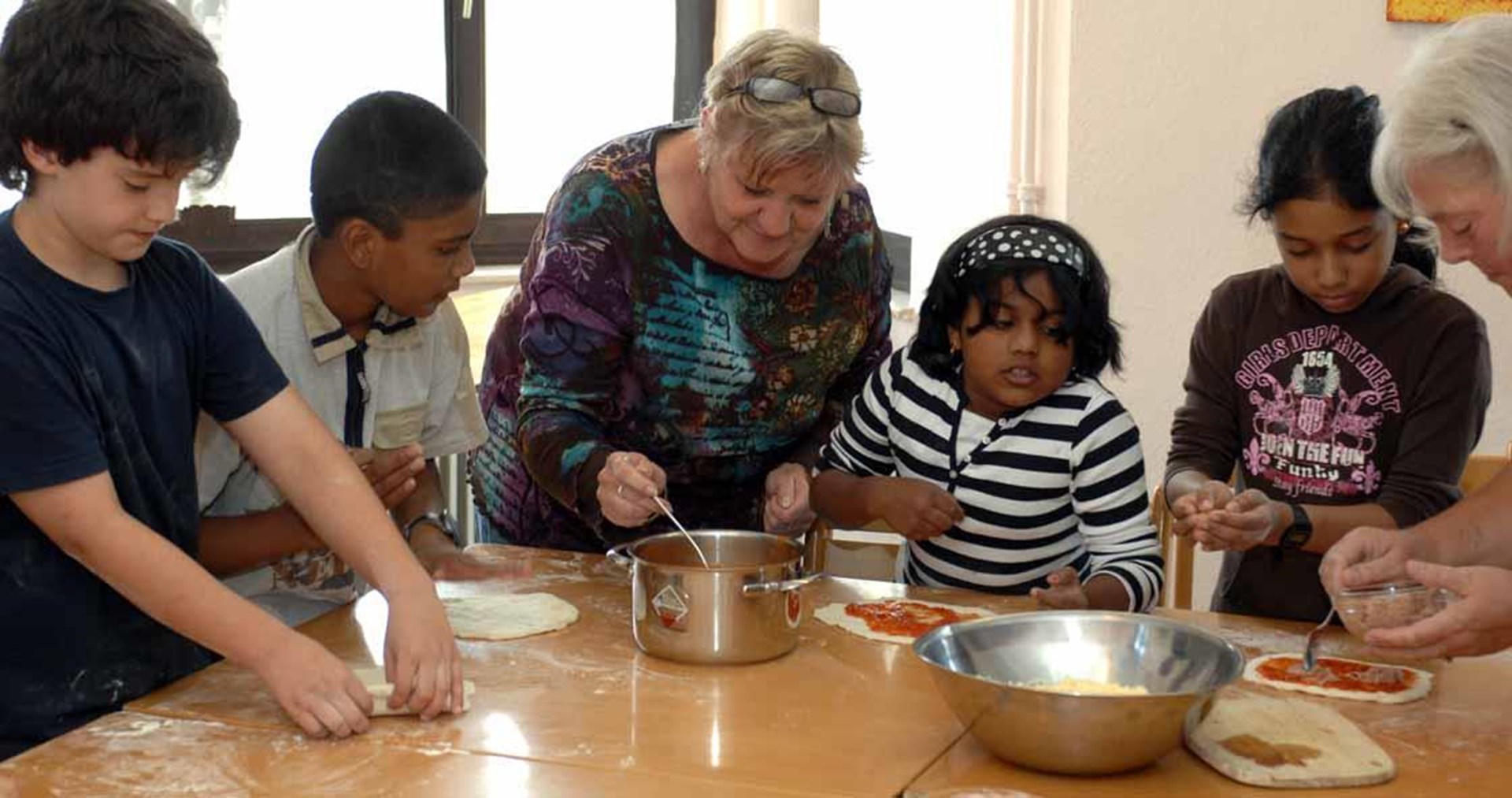 zwei Ehrenamtliche backen Pizza mit Kindern mit Migrationshintergrund